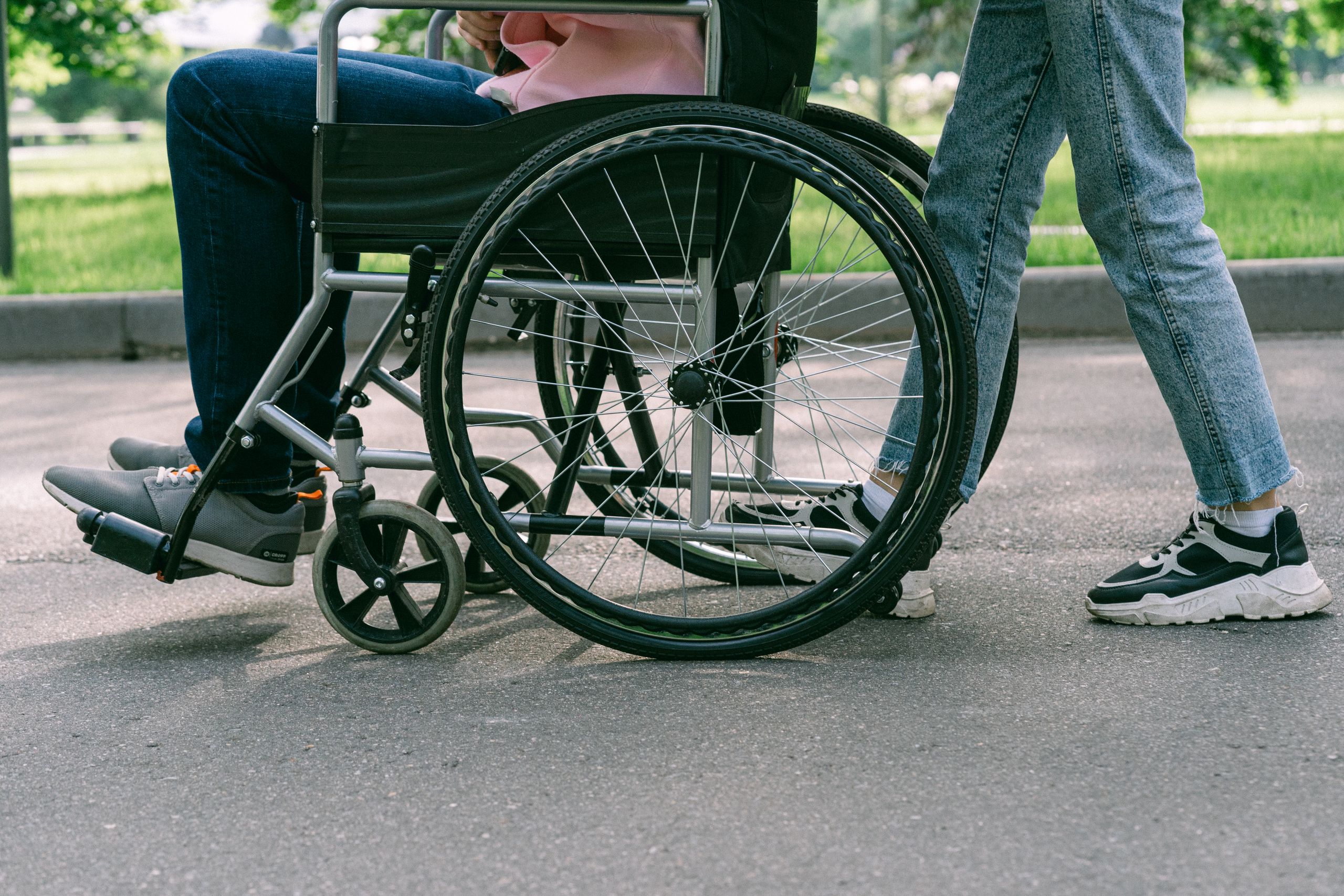 Close-up view of a person in a wheelchair being assisted on a sunny urban pavement.